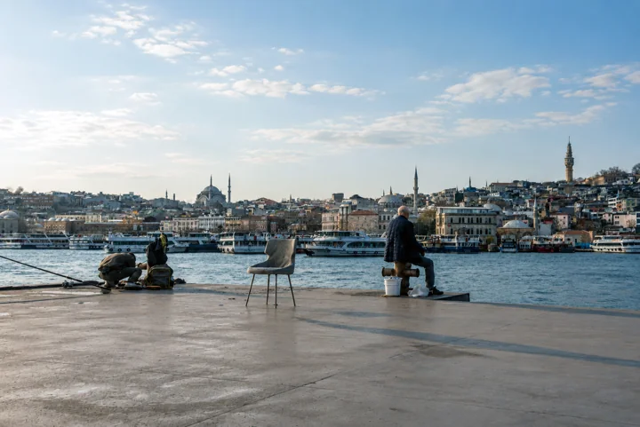 People fishing from a concrete waterfront with chairs and the city across the water