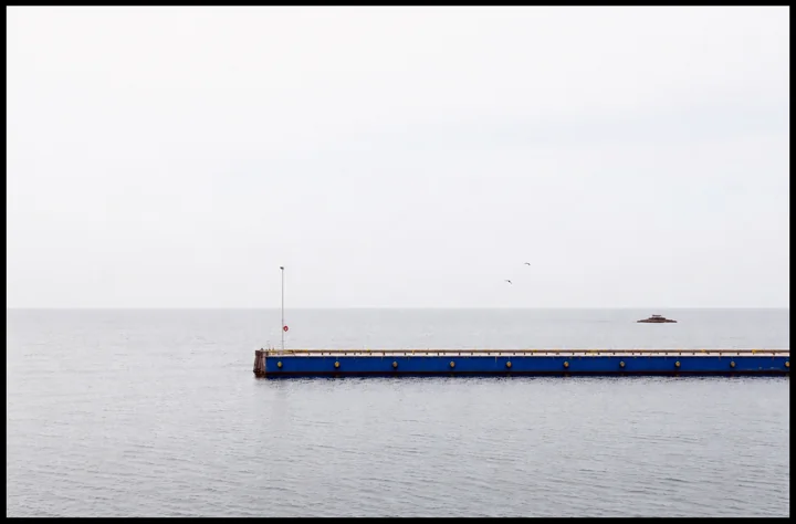 A blue jetty extending across pale water beneath an overcast sky