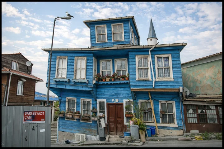 A blue wooden house with white trim beside other buildings