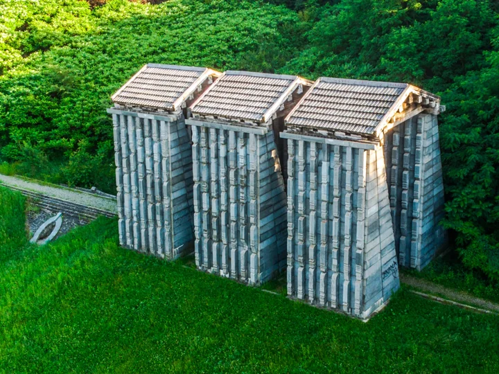 An aerial view of three ribbed concrete structures surrounded by green trees and grass