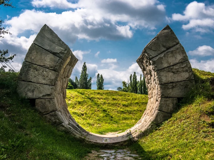 Two curved concrete forms enclosing an opening onto grass and trees